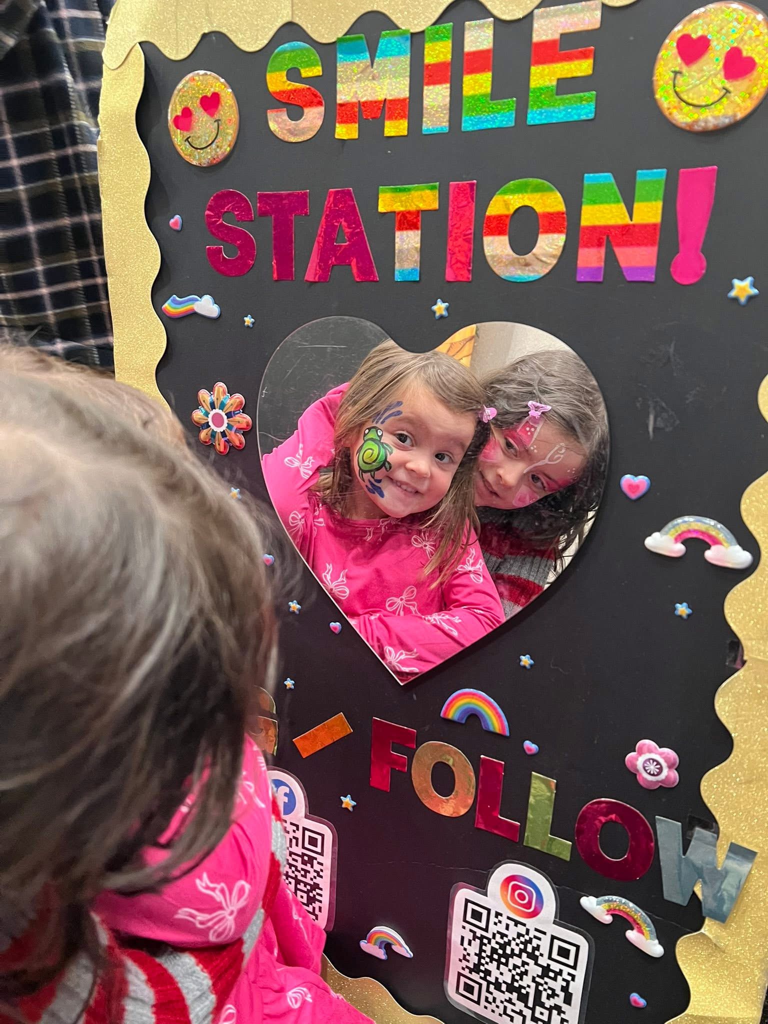 A child looking into the heart-shaped Smile Station mirror after getting her face painted